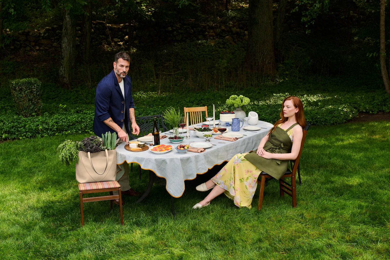 Two people beside a garden dinner table set with food, with an Atria tote resting on a chair.