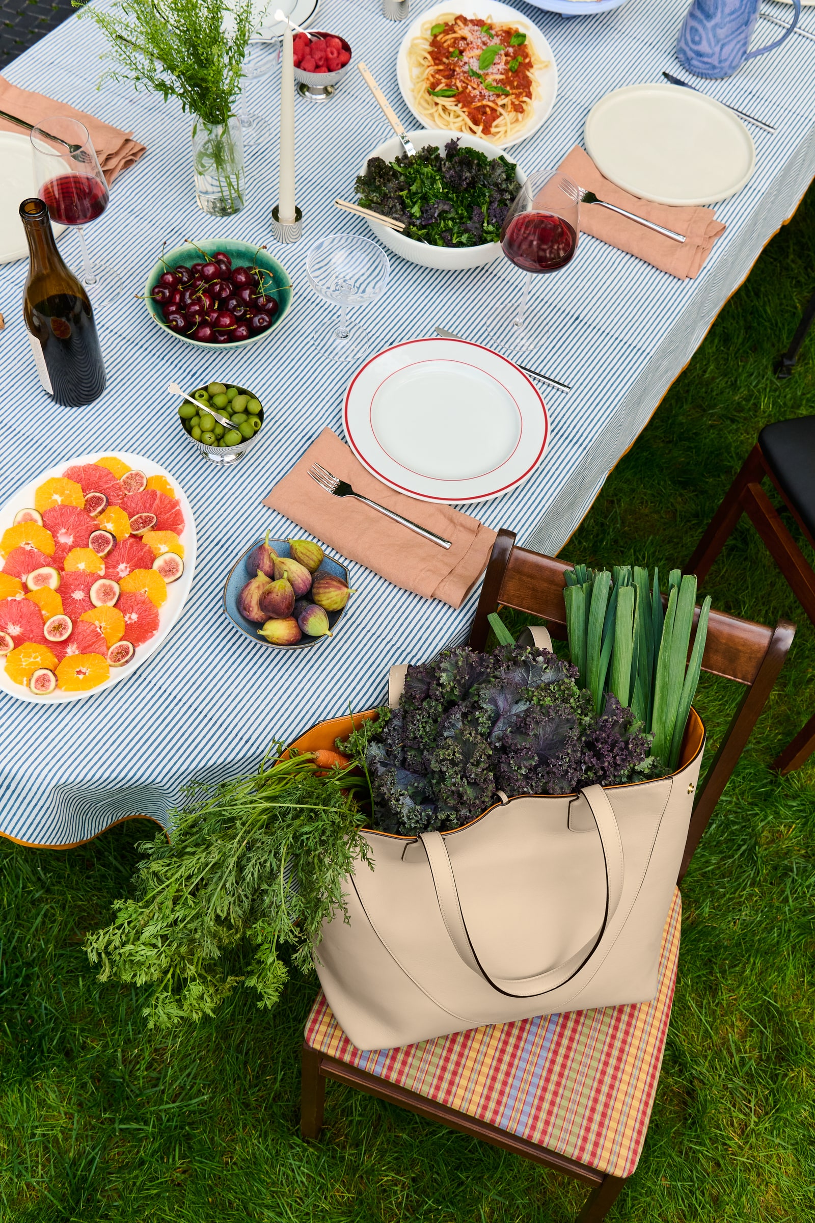 A garden table set for a meal, with an Atria tote and vegetables on a striped chair.