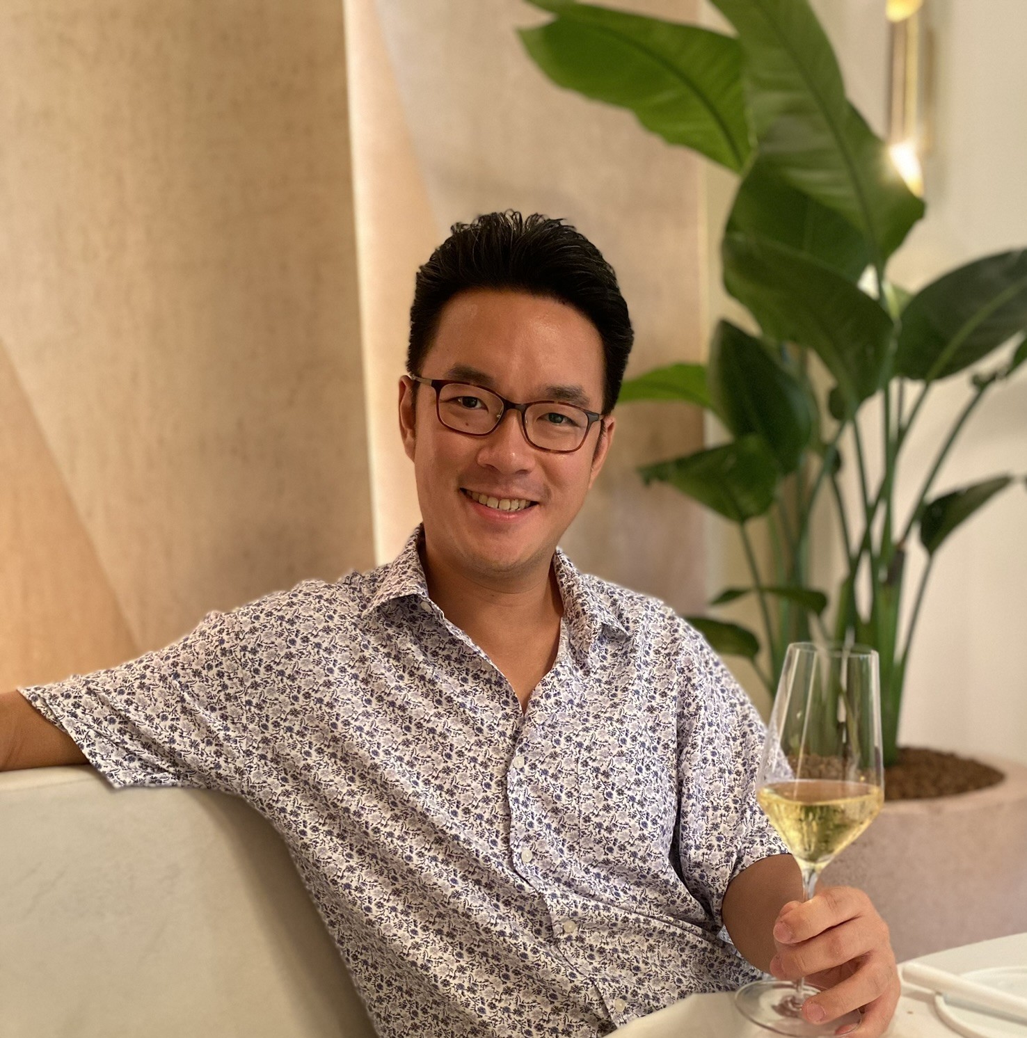 Zi Chan seated at a table, smiling and holding a glass of white wine.